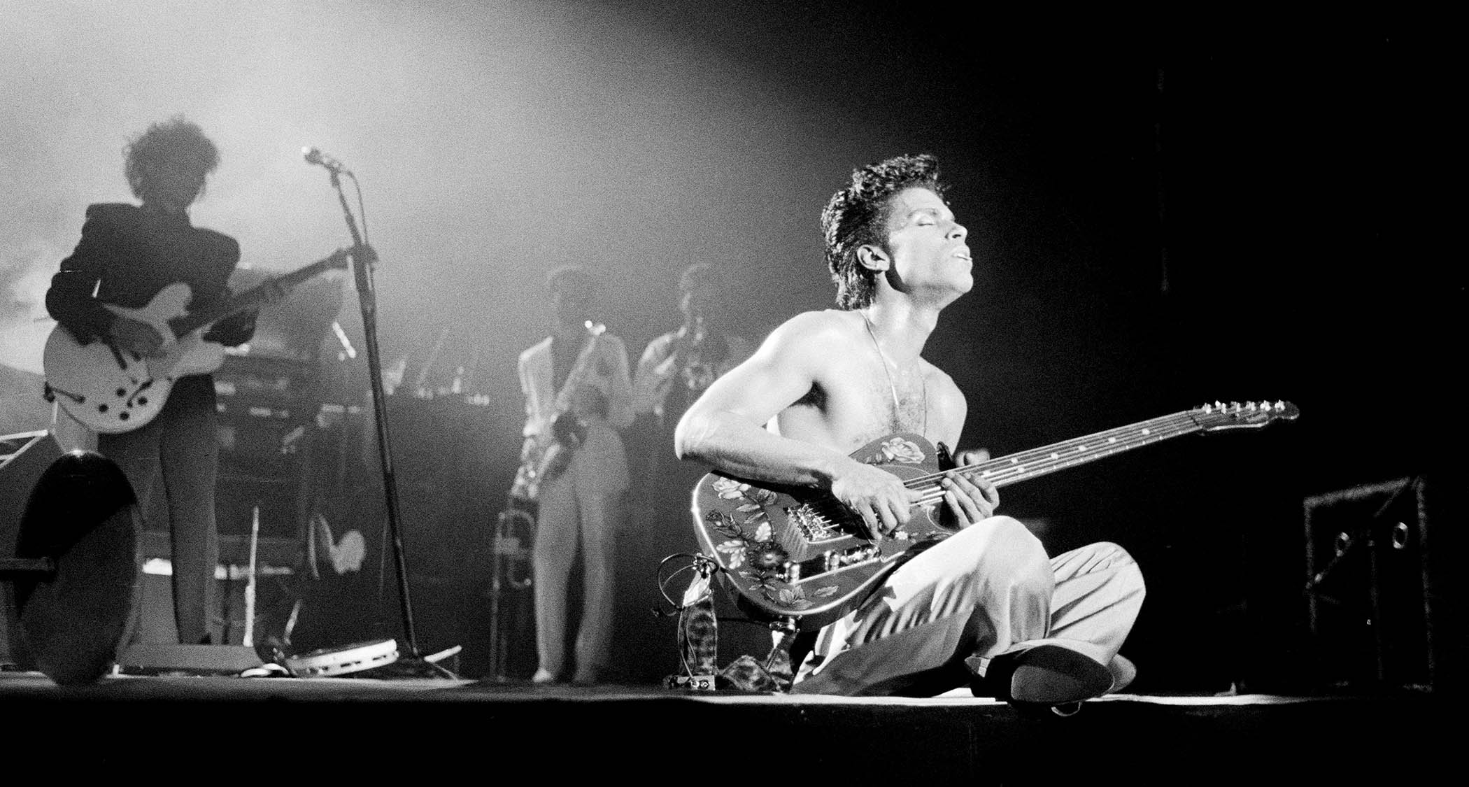 Prince sits cross-legged onstage and closes his eyes as he takes a guitar solo