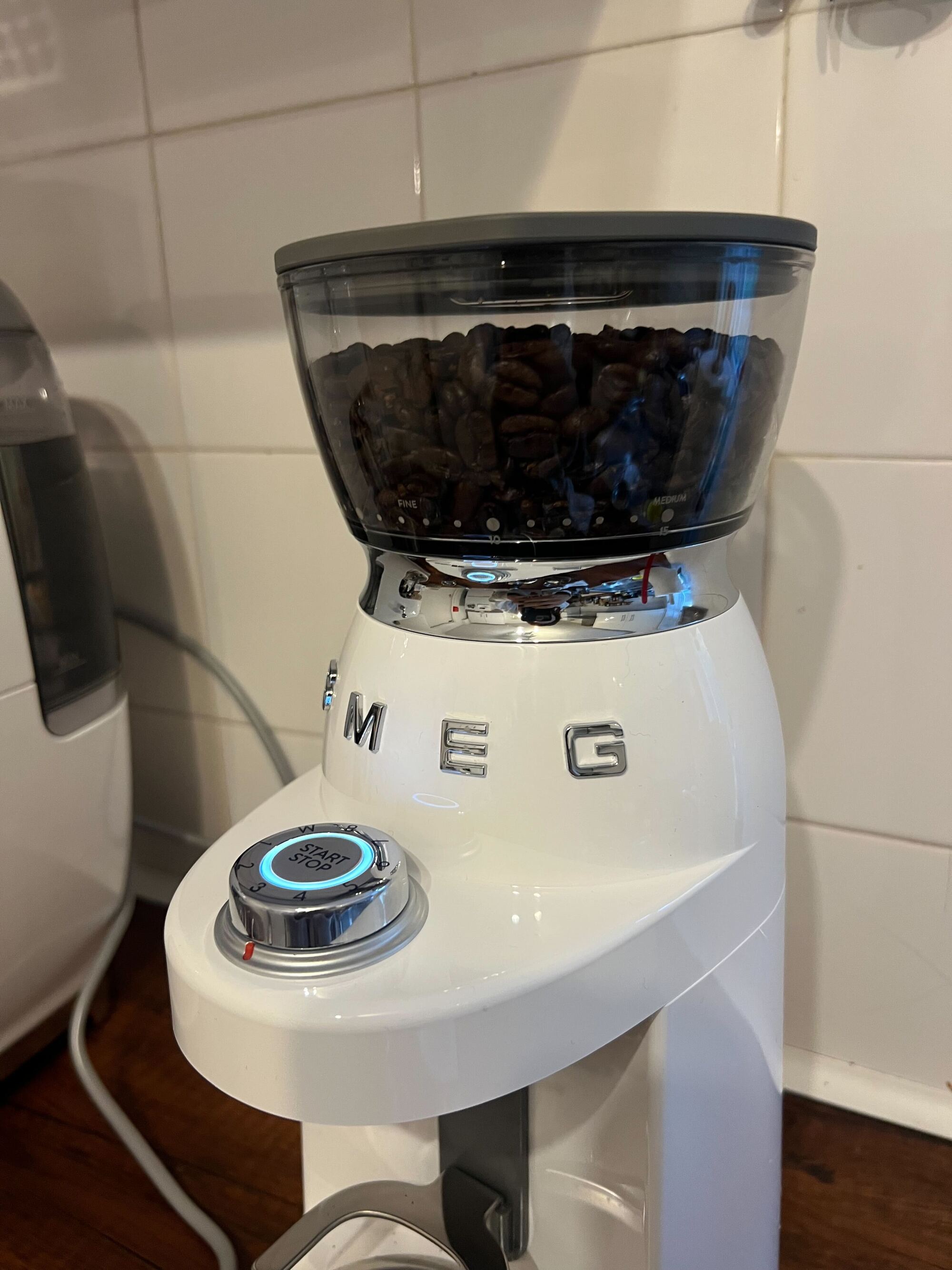 Image of a white Smeg coffee grinder on a wooden countertop with white tile backsplash