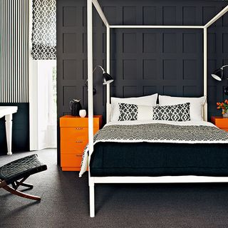 black bedroom with four poster bed cushions and orange cabinet
