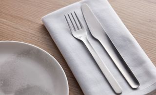 Stainless steel knife and fork on top of a folded white napkin