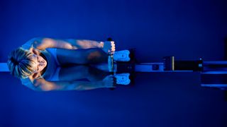 Birds-eye view of woman on rowing machine, bathed in a blue light