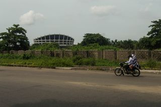 National Theatre, Lagos seen from a distance with moped with two passengers driving past