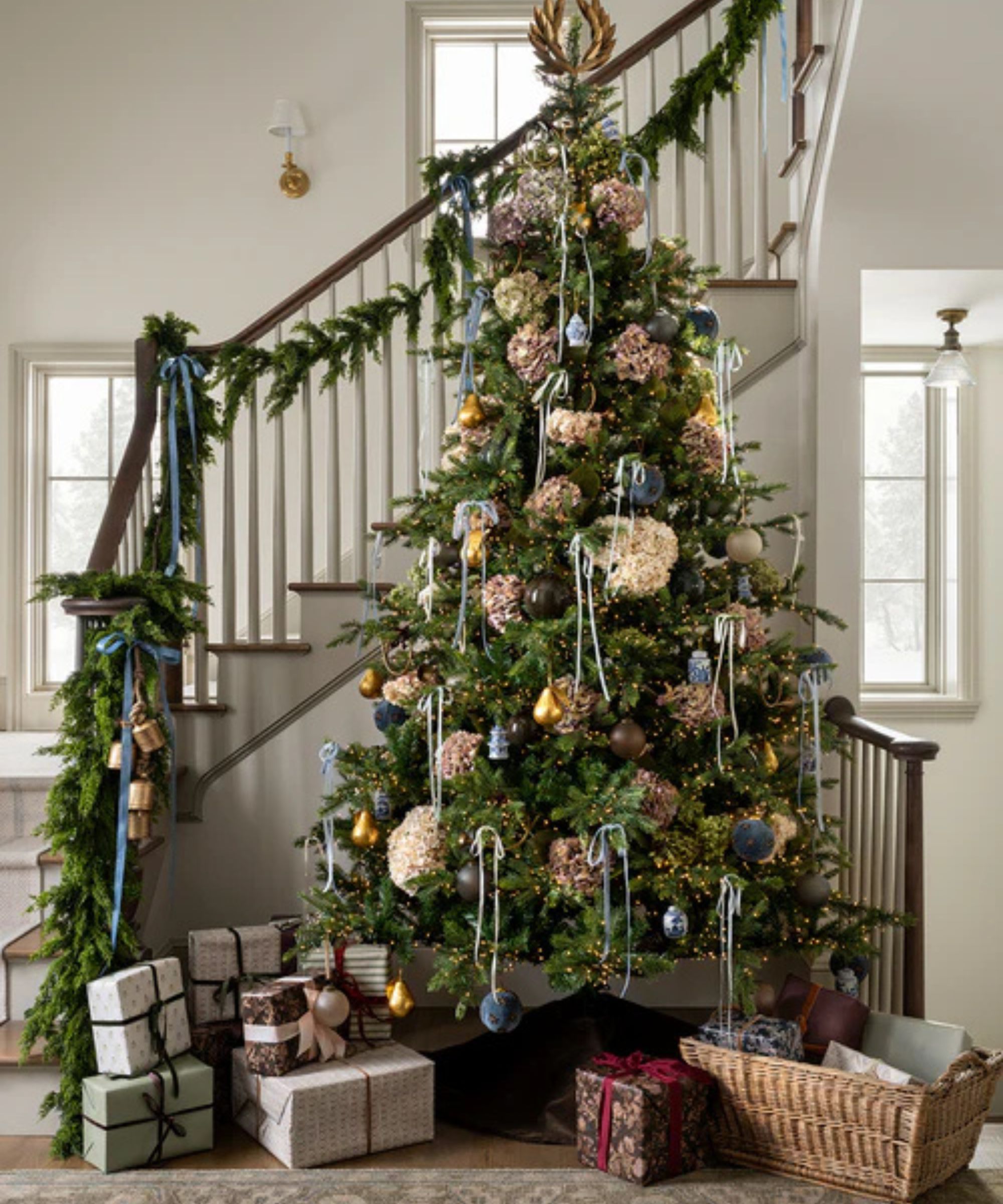 Entryway with a christmas tree decorated with hydrangeas and pale blue ornaments surrounded by presents