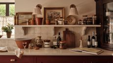 A kitchen with red cabinets, white worktops and white tile backsplash. Close up of the counter and a wall-mounted shelf covered in cozy kitchen clutter. 