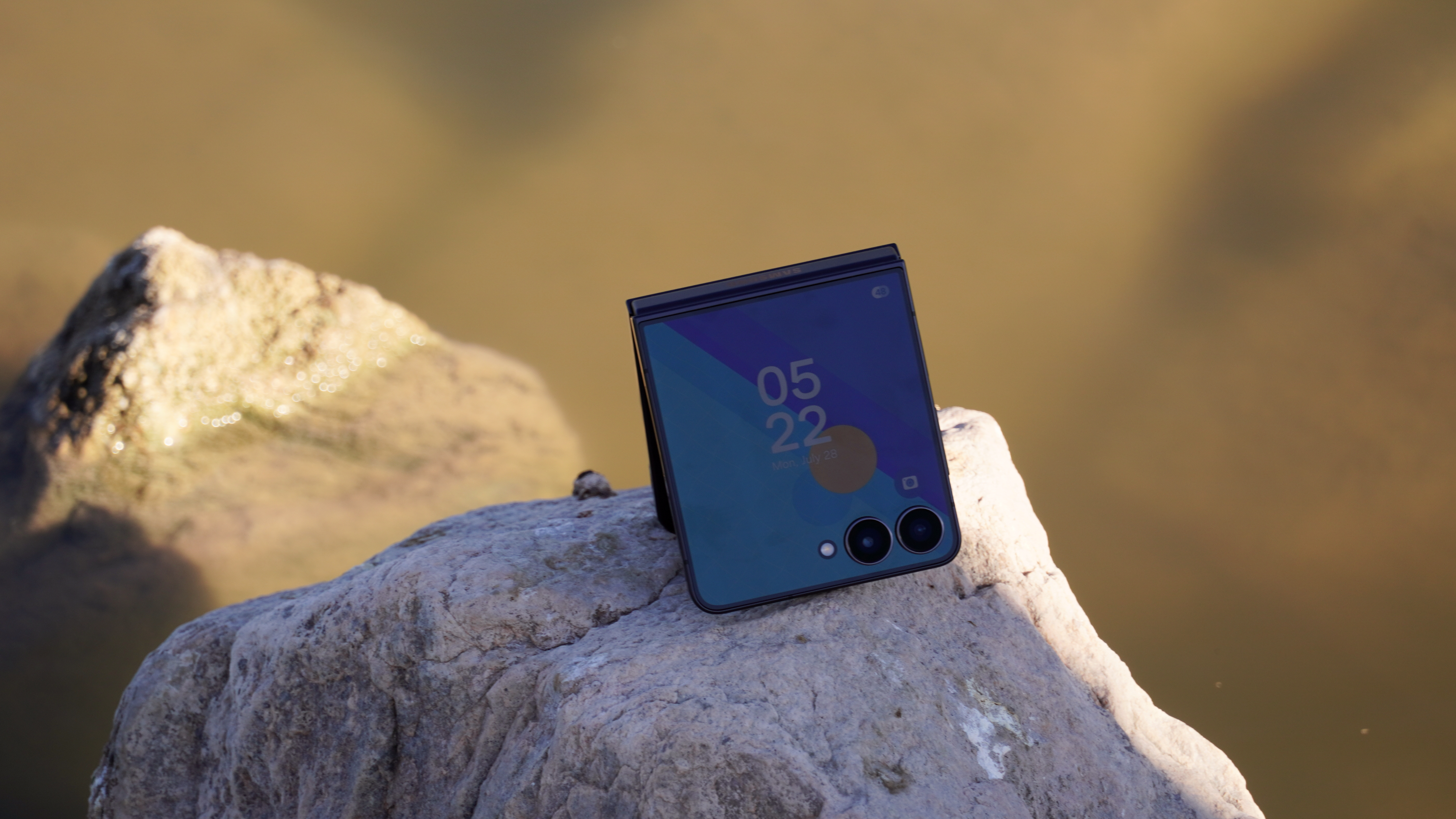 The Samsung Galaxy Z Flip 7 on a rock in a lake.