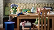 banquette seat with a scalloped fabric back rest with paisley print, oak table decorated with a cottagecore style and pillows with a small blue stool