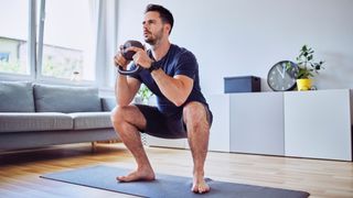 Man performs goblet squat at home using kettlebell