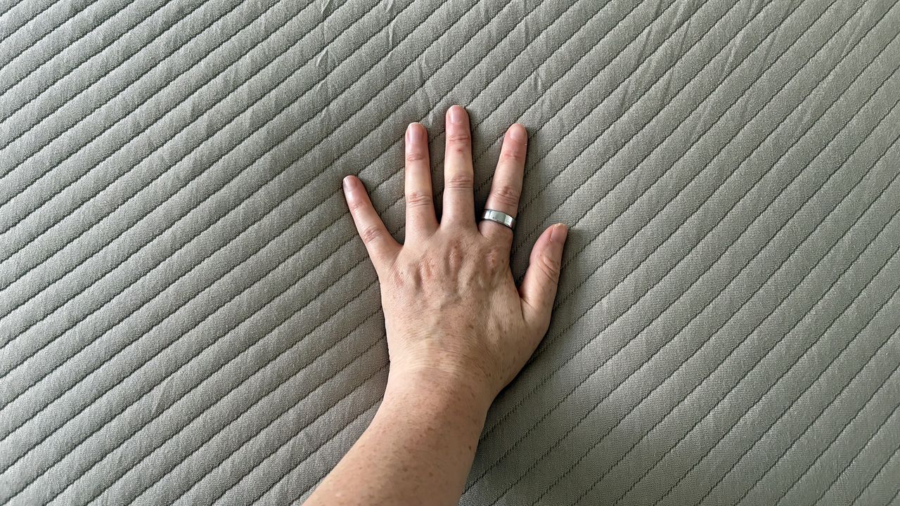 A close up of our reviewer's hand touching the surface of the Orion Sleep System to check the feel