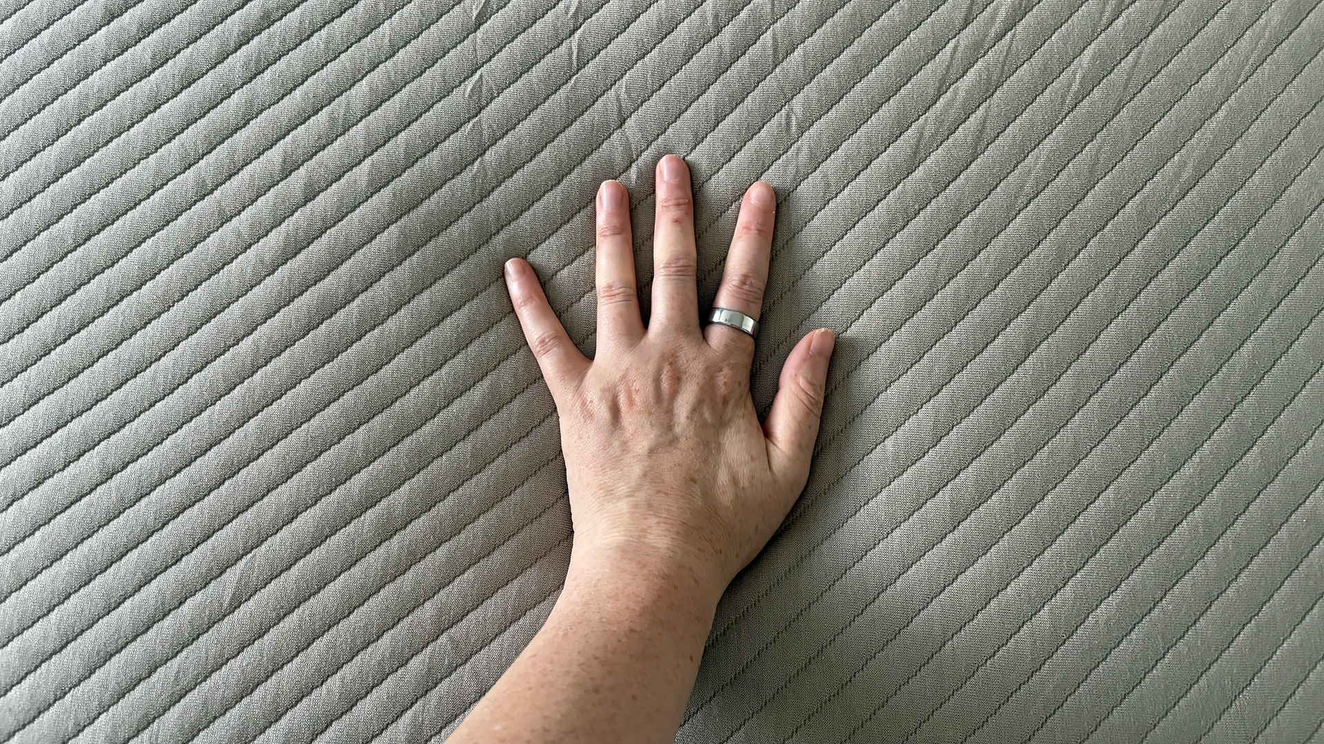 A close up of our reviewer's hand touching the surface of the Orion Sleep System to check the feel