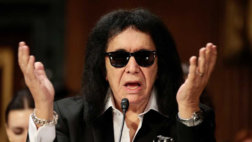 Gene Simmons in sunglasses waving his hands in the air