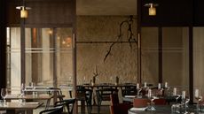 A brutalist restaurant's dining room with cracked cement walls, mid-century modern leather and wood furniture, softly glowing lighting, and wine glasses.