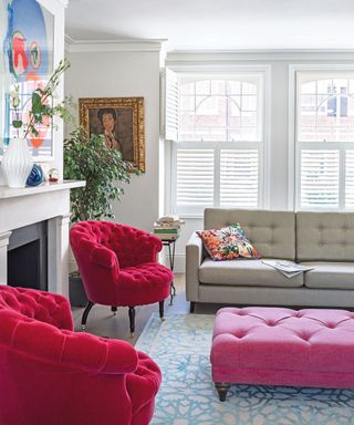 A white living room with shocking pink furniture, a blue geometric patterned rug and modern art.