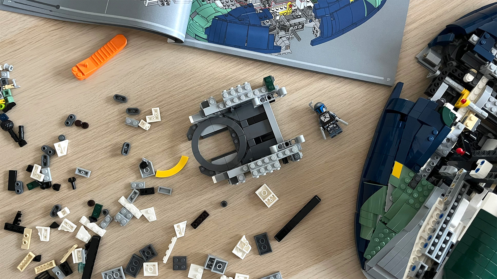 Lego Star Wars UCS Jango Fett&rsquo;s Firespray-Class Starship (75409) mid-build on wooden tabletop next to lots of Lego pieces and an instruction booklet 