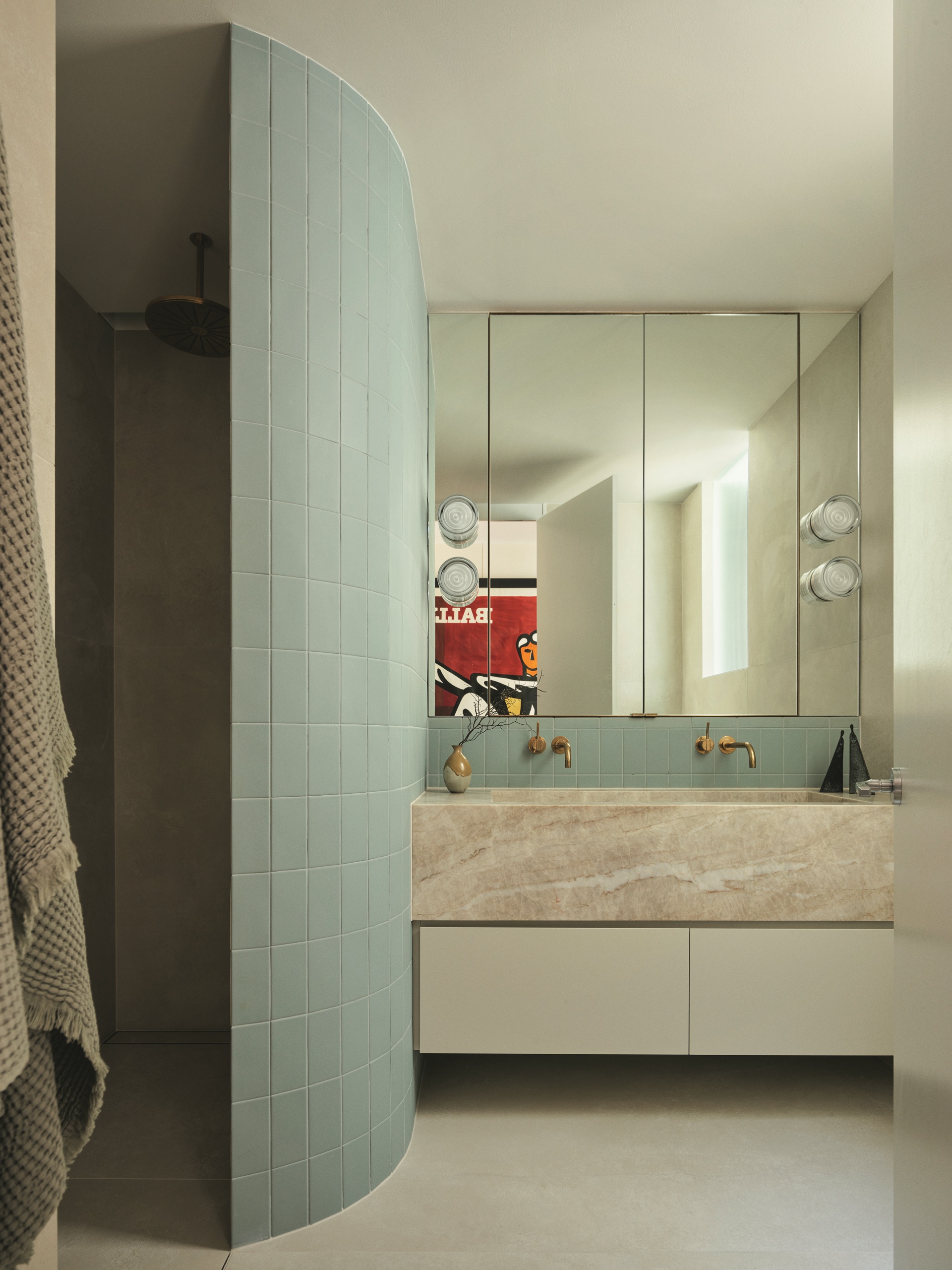 modern bathroom with curved wall in green tiles, floating marble vanity with sage green cabinets, mirrored wall with in-built cabinets, brass taps and wall sconces