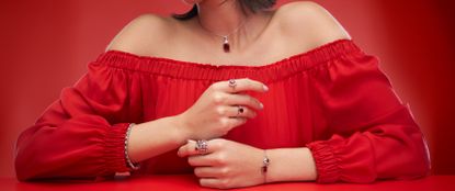 Model on red background wearing a red off the shoulder dress and red gemstone jewellery sold at Angara