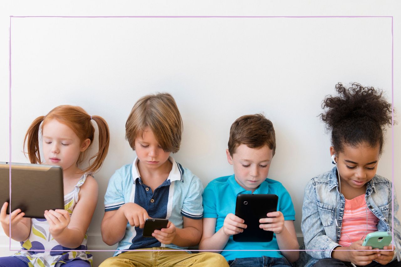 Four children sat against a wall watching a variety of screens