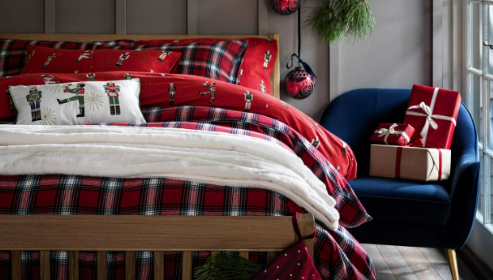 A red-and-white check bedding set from M&S on a double bed, with a blue chair to the side and some wrapped presents.