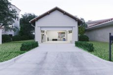 A driveway leading to an empty garage of a home with the door open. 