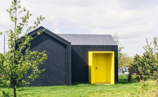 The wooden shacks which are to inhabit the space are elementary in form, like prefabricated slabs of sorts, and decorated with vivid yellow doors and windows seemingly punching out from the otherwise quite plain architecture
