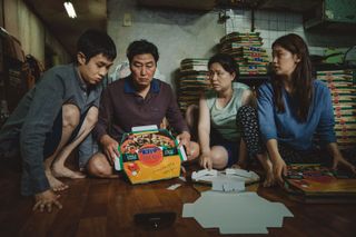 a family sits on the ground around folded pizza boxes in 'Parasite'