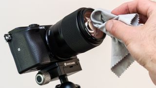 A hand using a cloth to clean a camera lens