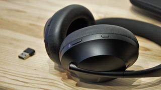 Ett par svarta Bose 700 UC Noise Cancelling Headphones ligger på ett träfärgat bord med sin USB-C-sticka bredvid.
