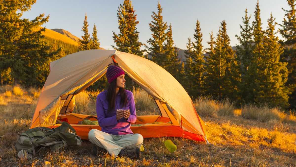 A woman sitting outside her tent drinking tea