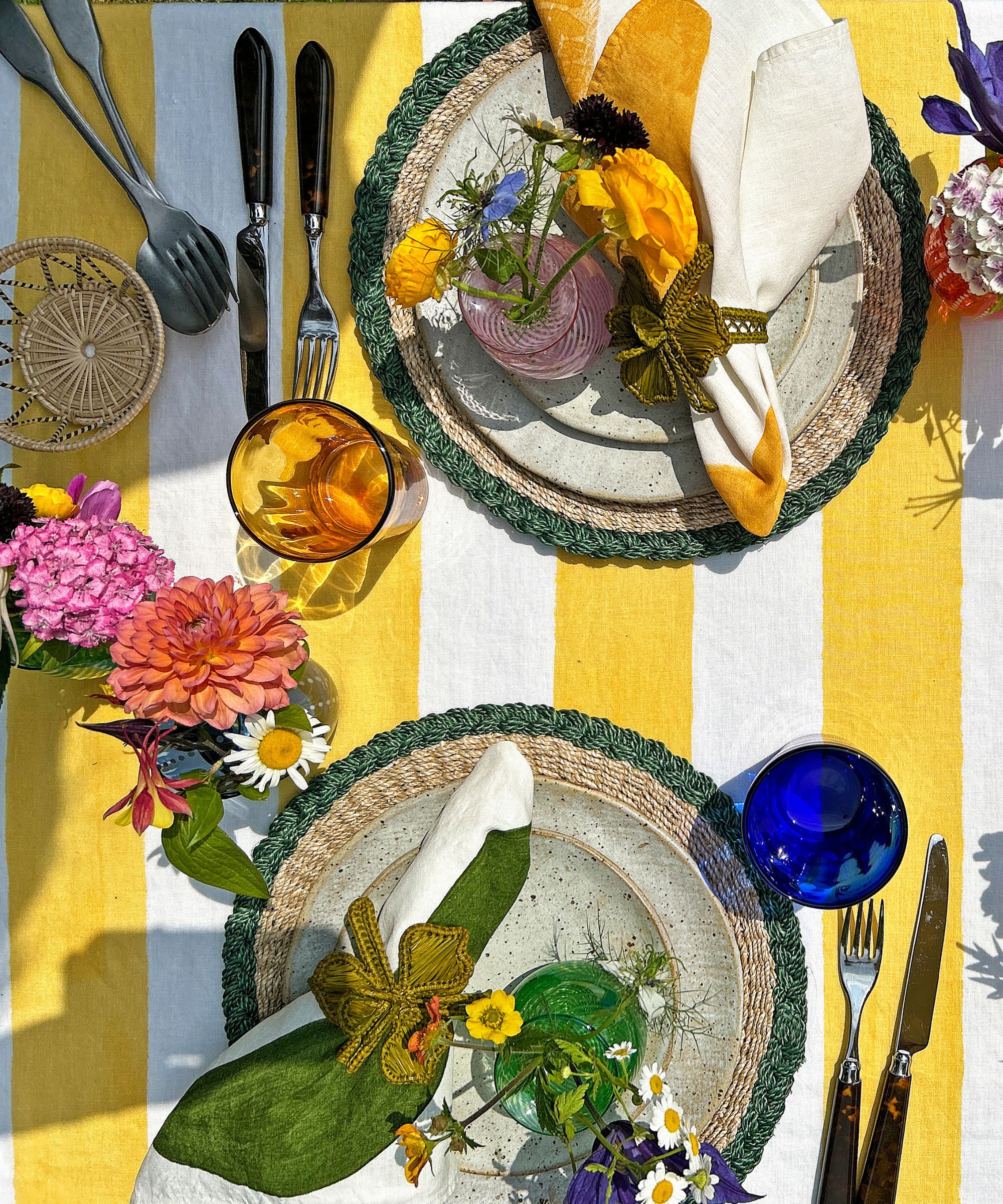 Yellow and white stripe tablecloth with plates, napkins and colored glasses set on it, with vases of flowers