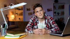 Teenage boy in bedroom holding cash and thinking about it 