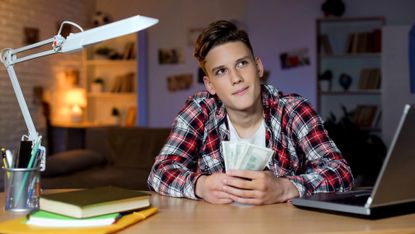 Teenage boy in bedroom holding cash and thinking about it 