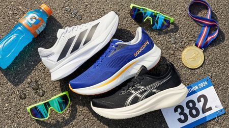 Saucony Ride 19, Adidas Duramo and Asics Gel-Nimbus shoes on asphalt surrounded by running gear