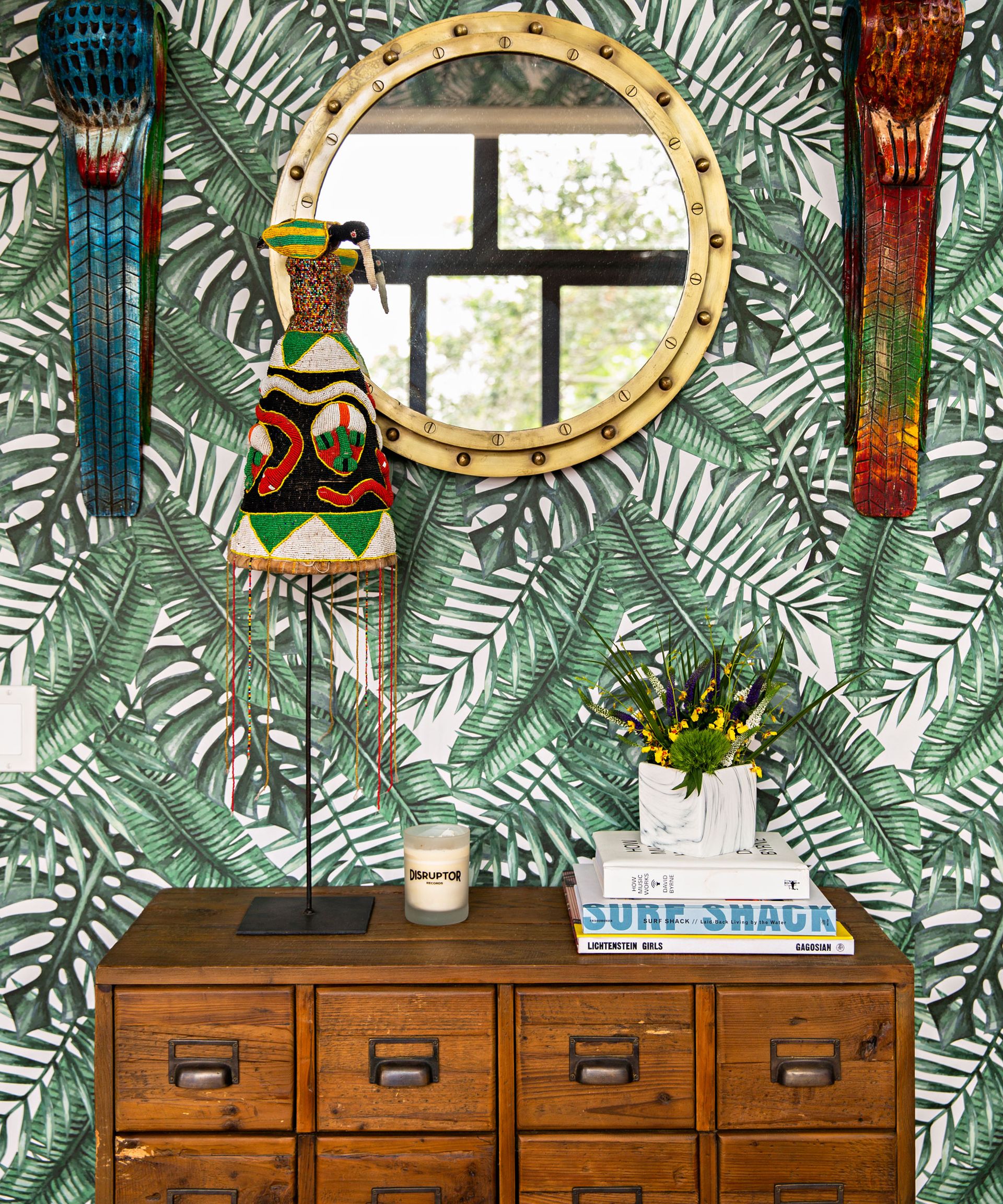 Vintage wooden chest, verdant jungle wallpaper, and porthole style brass, round wall mirror.