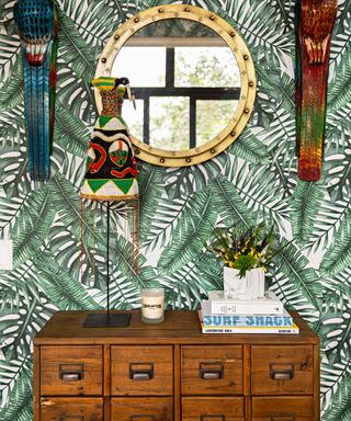 Vintage wooden chest, verdant jungle wallpaper, and porthole style brass, round wall mirror.