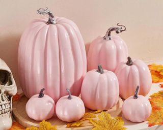 A collection of light pink pumpkins with orange fall leaves in front of them