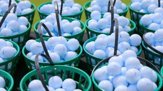 Driving range balls in green buckets lined up next to eachother