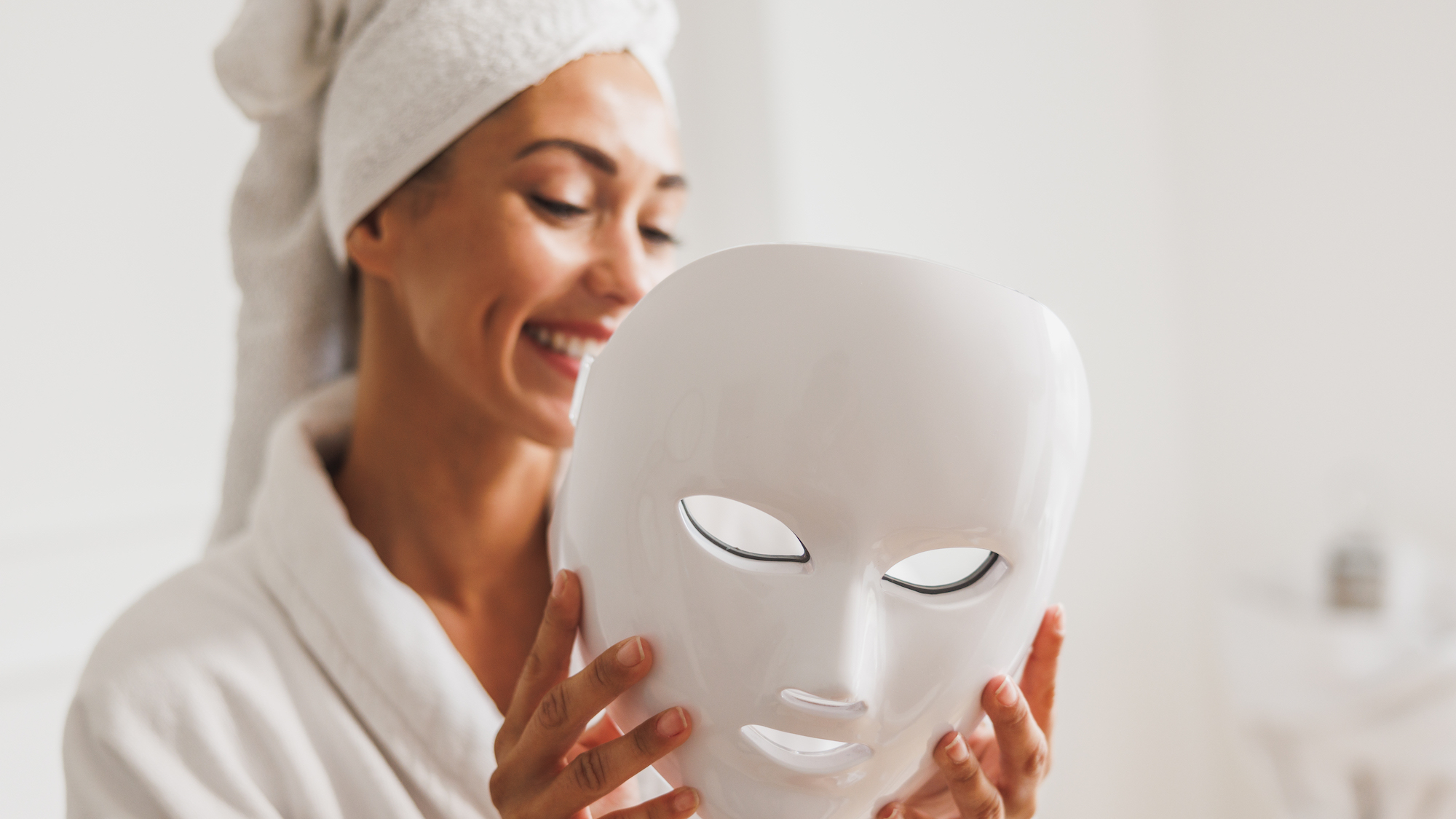 woman wearing hair towel and robe holding led face mask - the best beauty tech to buy at amazon