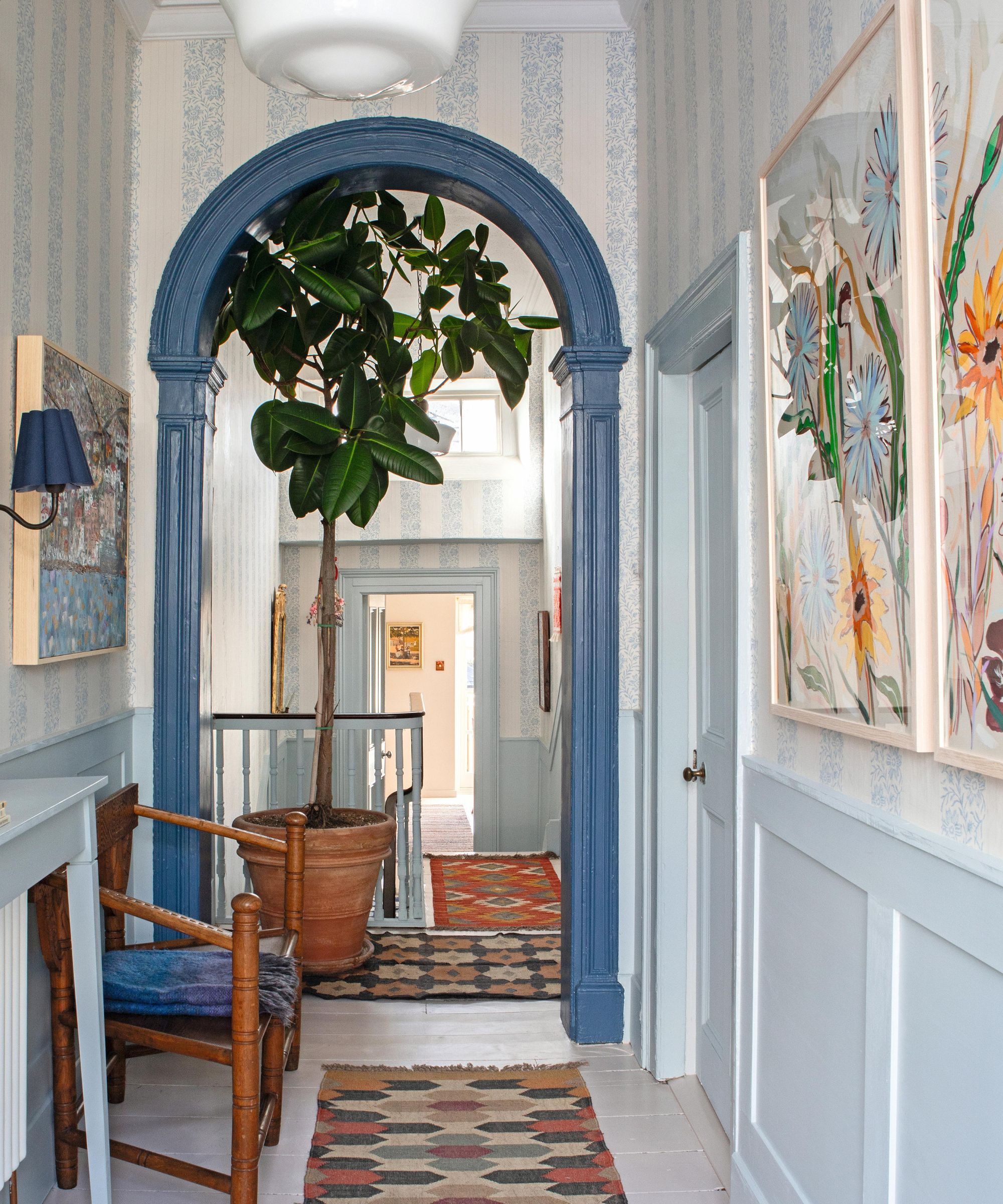 a Victorian entryway with floral striped wallpaper, light blue half paneling, a mid blue painted arched walk way and layered vintage runner rugs