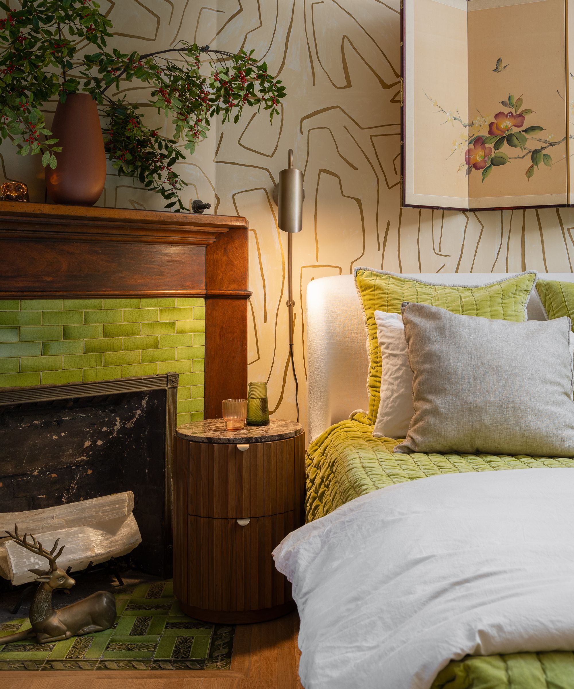Bedroom corner with a bed in white and lime green, a round wood nightstand, and a fireplace with bright green tiled surround