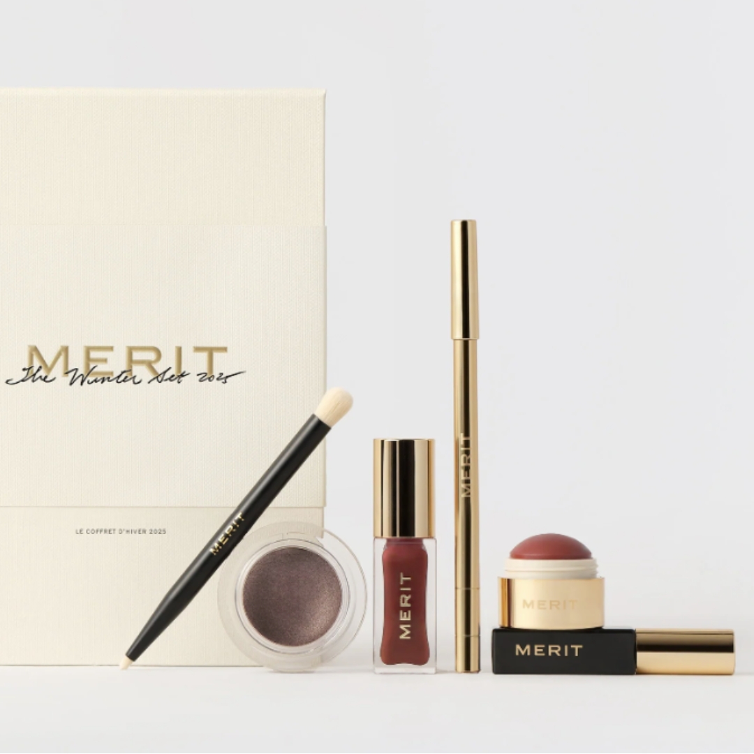 A product shot of Merit&#039;s The Winter 2025 Set, which features the limited edition Shade Slick Sheen in Courmayeur, the Signature Lip Liner in Courmayeur, the Mini Flush Balm in Courmayeur, the Mini Clean Lash in Perfect Black, the Solo Shadow Sheen in Mink (soft brown grey) and finally the Brush No. 2/ all pictured on a grey background, alongside the cream gift box packaging.