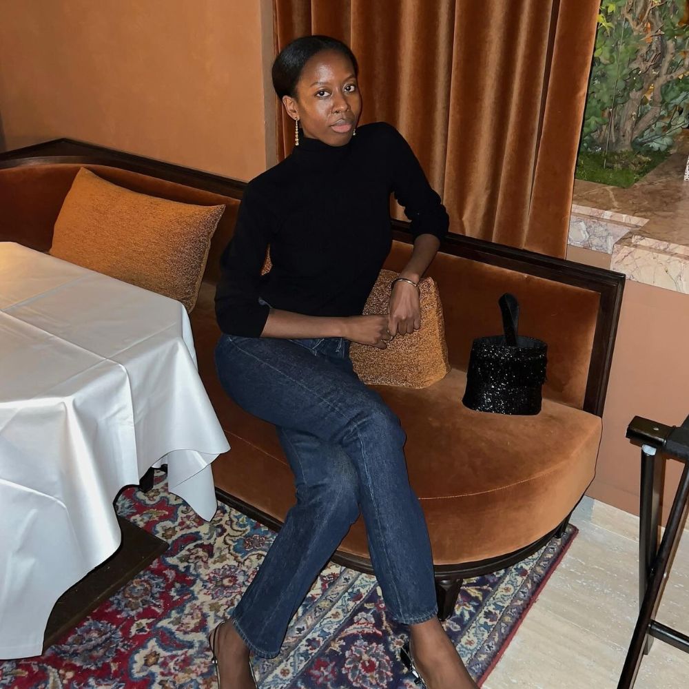 Influencer @sylviemus_ sits in a restaurant wearing indigo cigarette jeans with black pointed-toe slingback shoes and a black turtleneck.