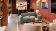 A flooring showroom with terracotta-colored walls, a stone backsplash bar area, a living room with green and pink sofa seats, and framed prints on the wall