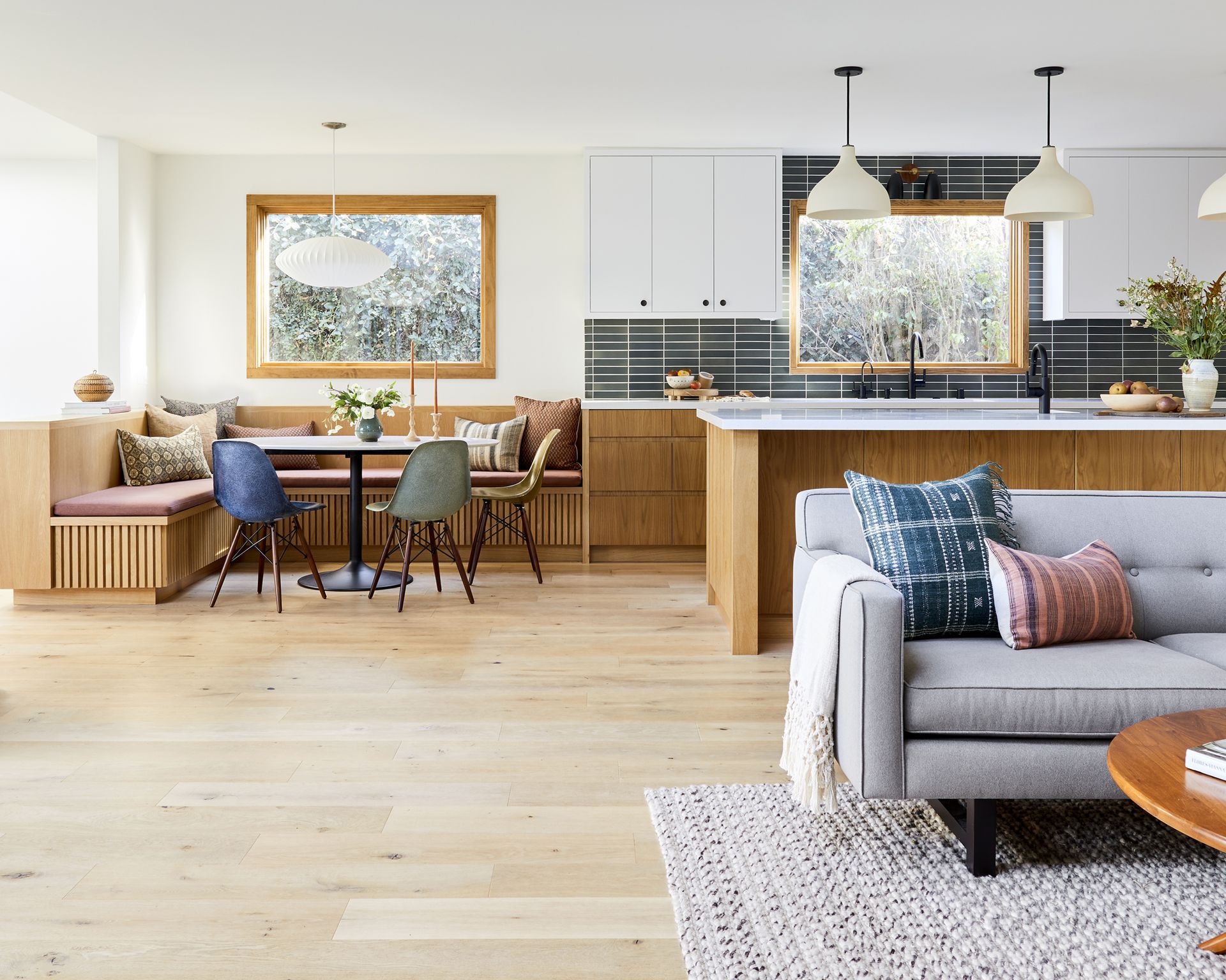 A kitchen with white pendant lights over the white oak island and breakfast area