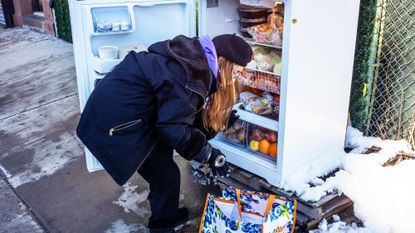 woman in snow in front of community fridge