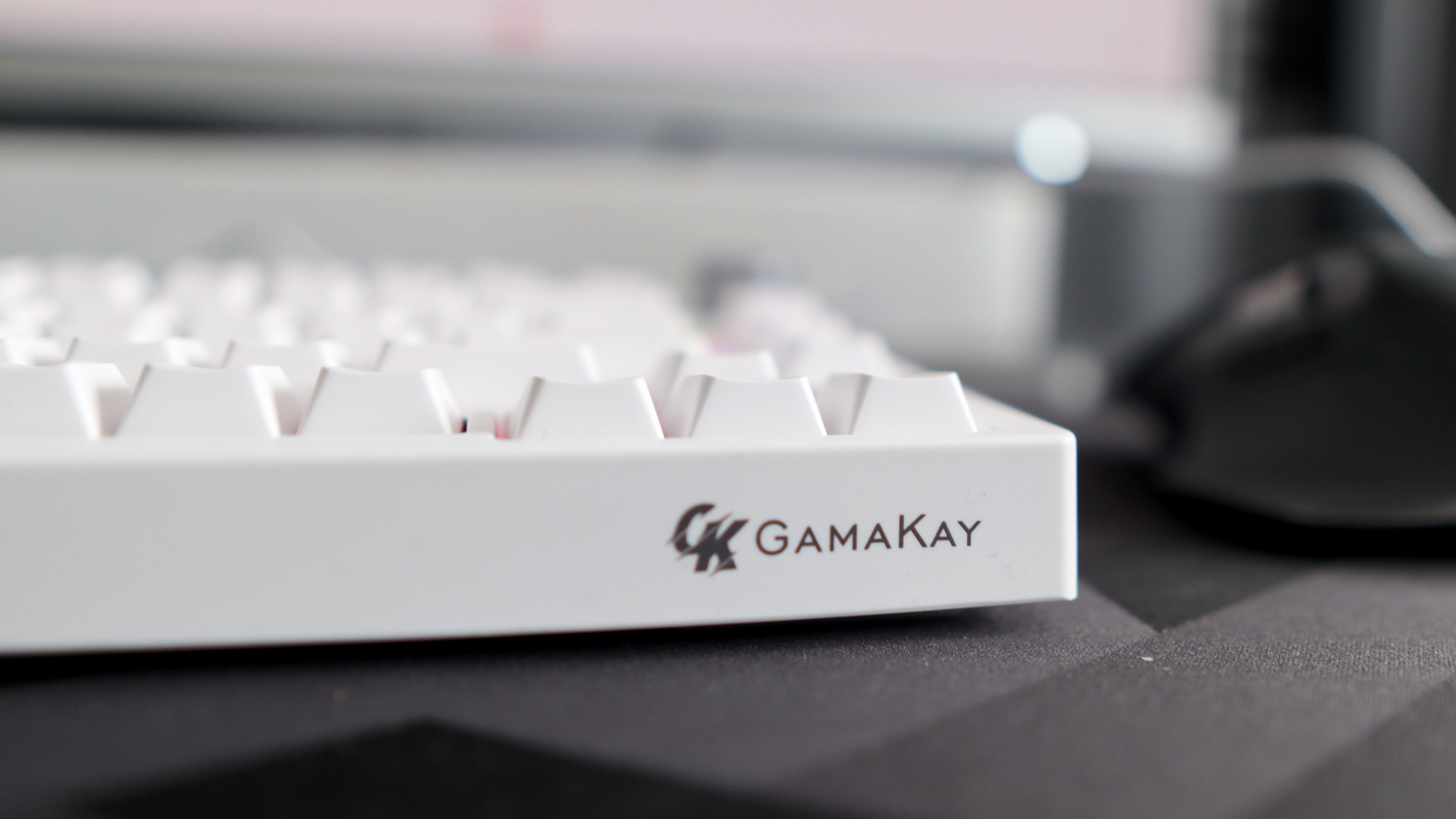 A Gamakay TK75HE gaming keyboard in white on a black and grey mouse pad with RGB lighting enabled.