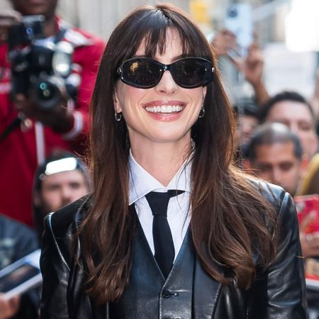 Anne Hathaway wearing a black leather three-piece suit with a tie and black flower-detail pumps