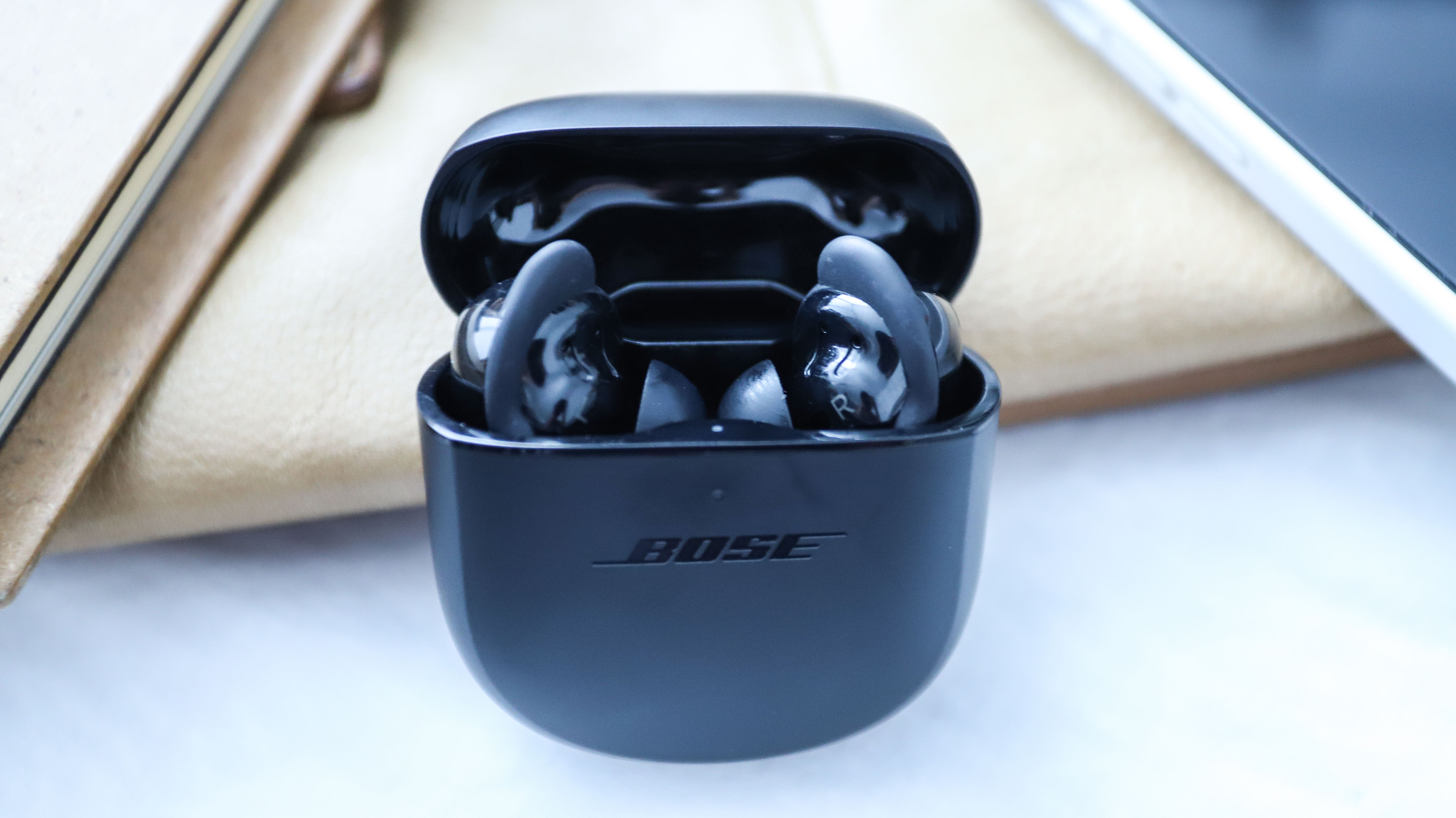 Ett par svarta Bose QuietComfort Earbuds 2 ligger inuti ett öppnat laddningsfodral.