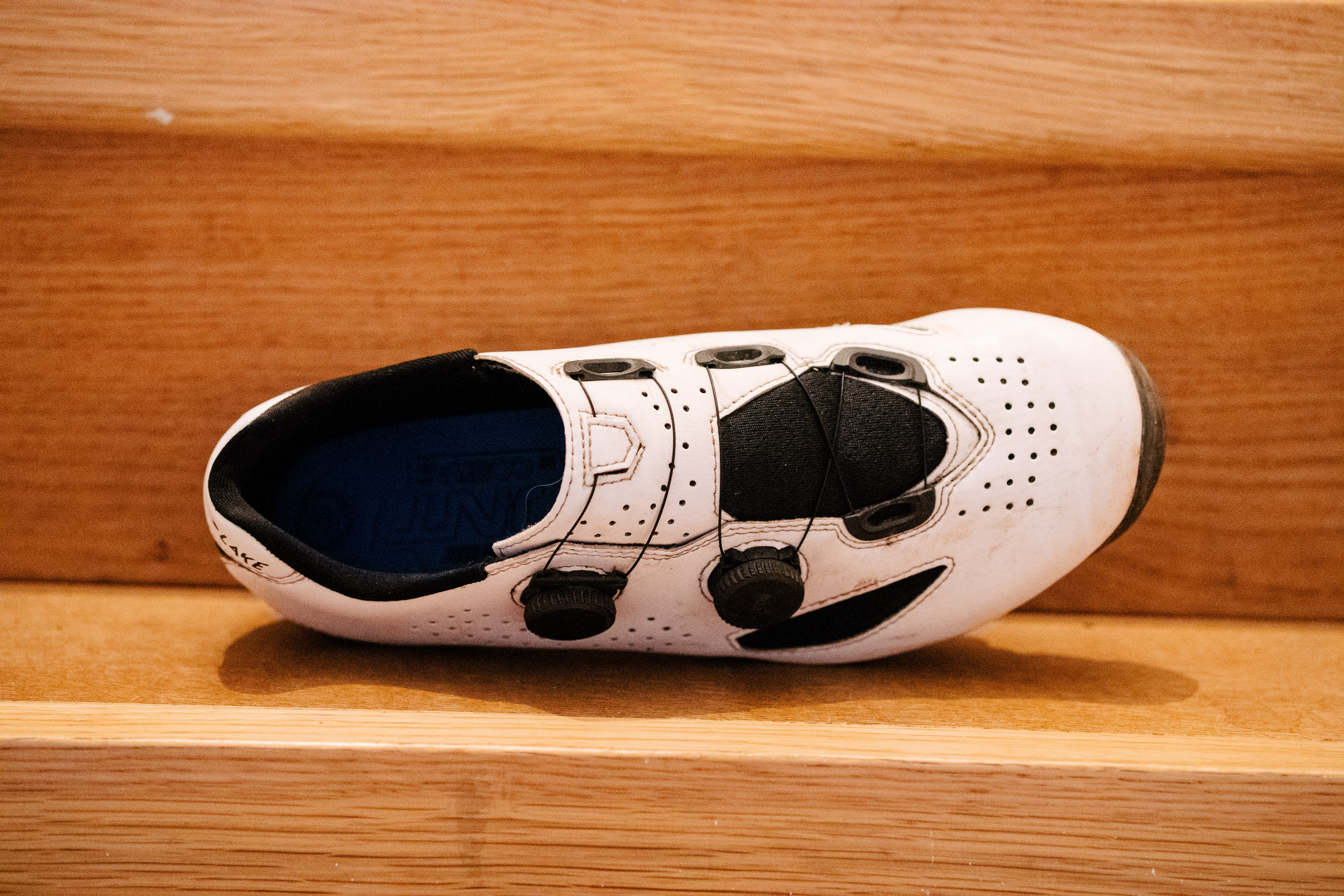 A white gravel bike shoe on wooden stairs