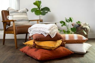 Orange, yellow, and cream cushions with a blanket stacked on top of each other.