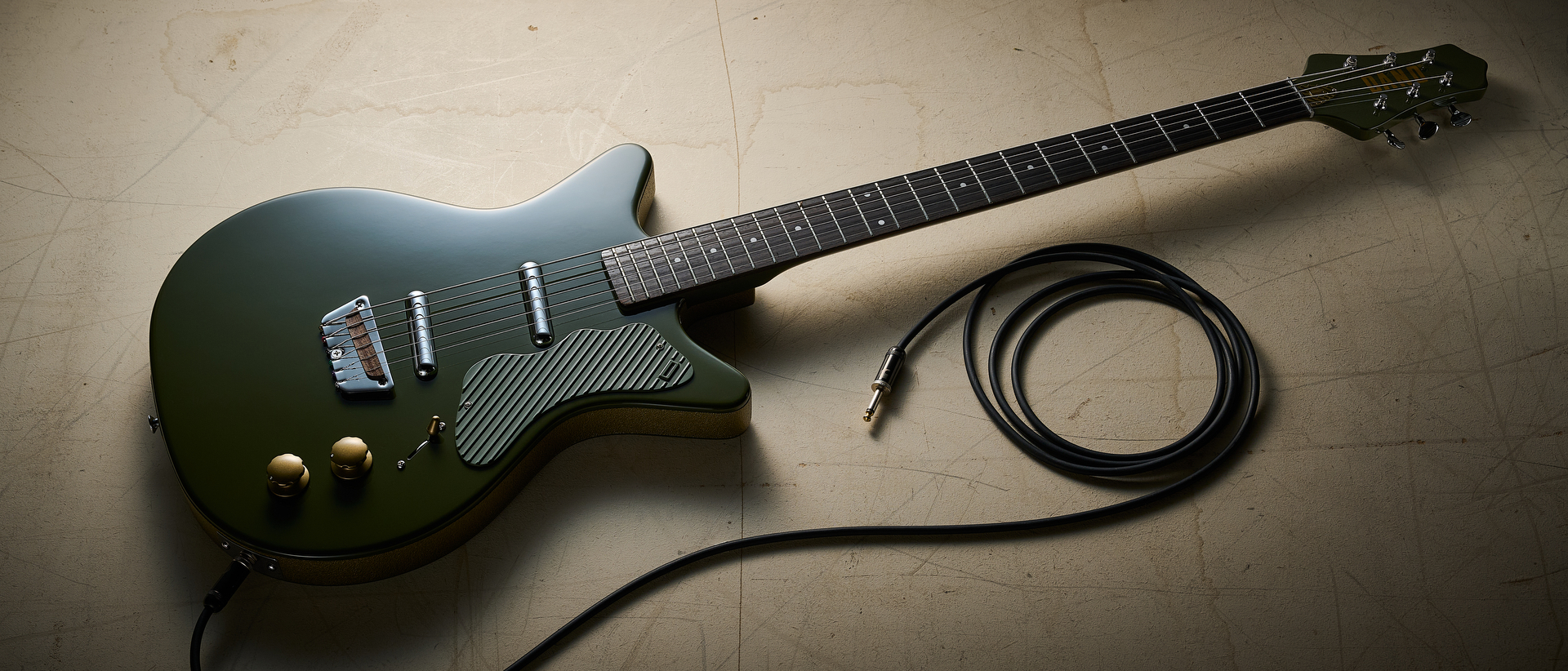 A Danelectro Dan O Cool Baritone guitar on an off white floor with a guitar cable nearby