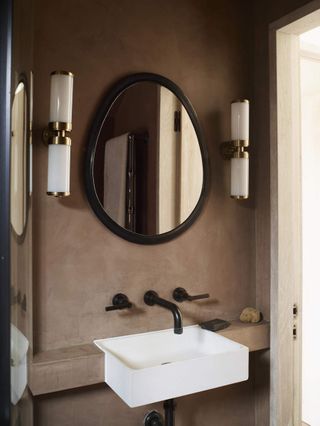 A dark plastered bathroom sink with a round mirror